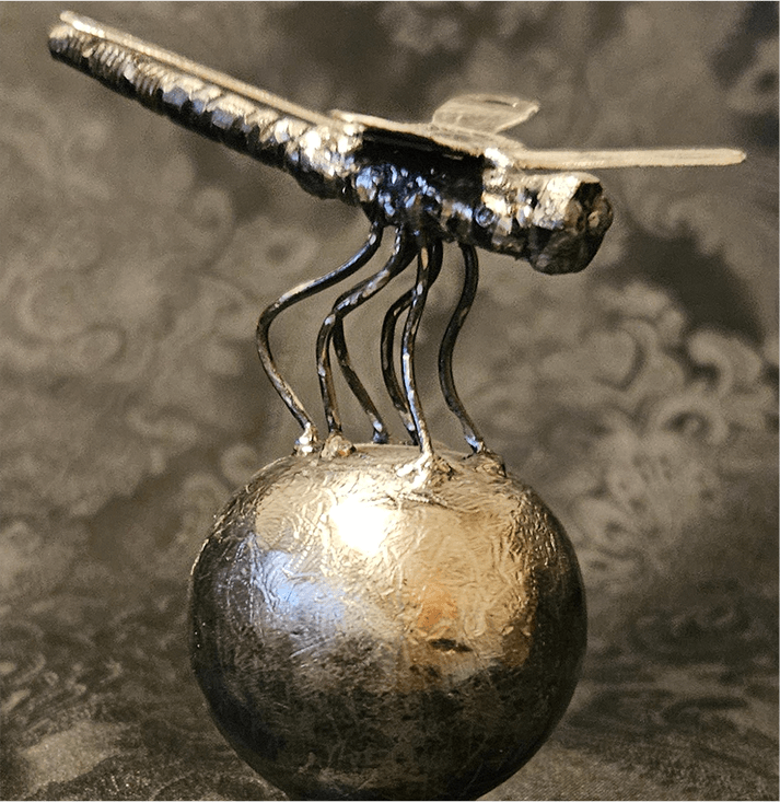 A metal sculpture of an insect on top of a ball.