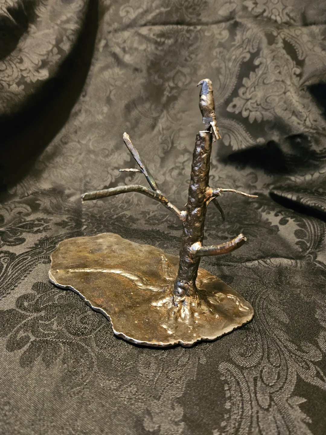 A metal sculpture of a tree on top of a leaf.