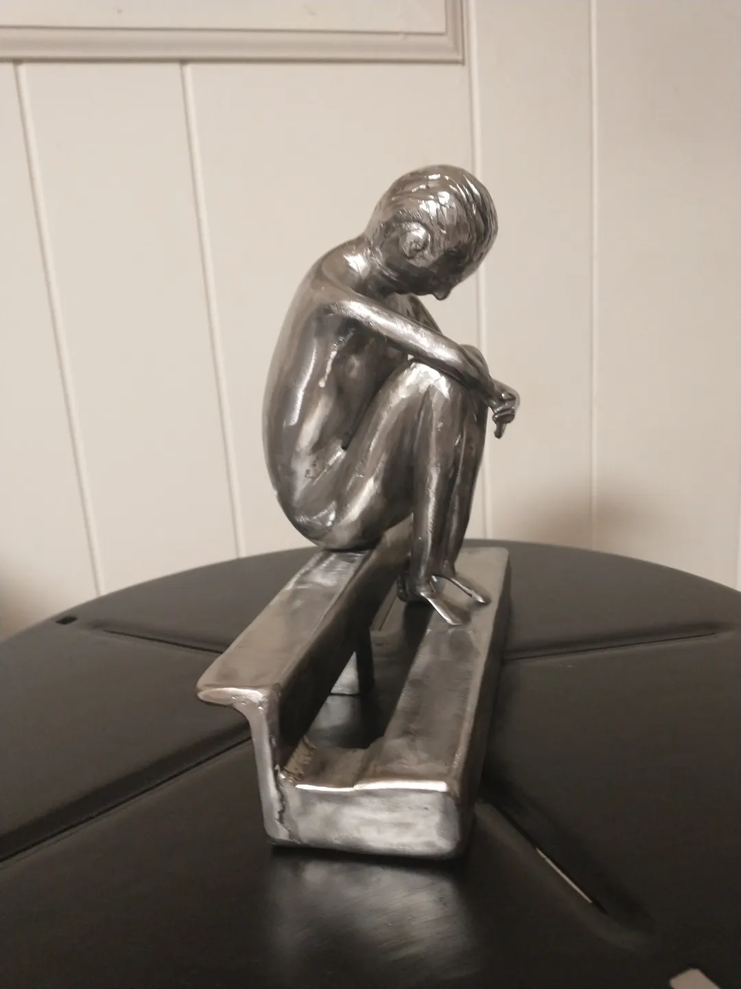 A silver statue of a man sitting on top of a bench.