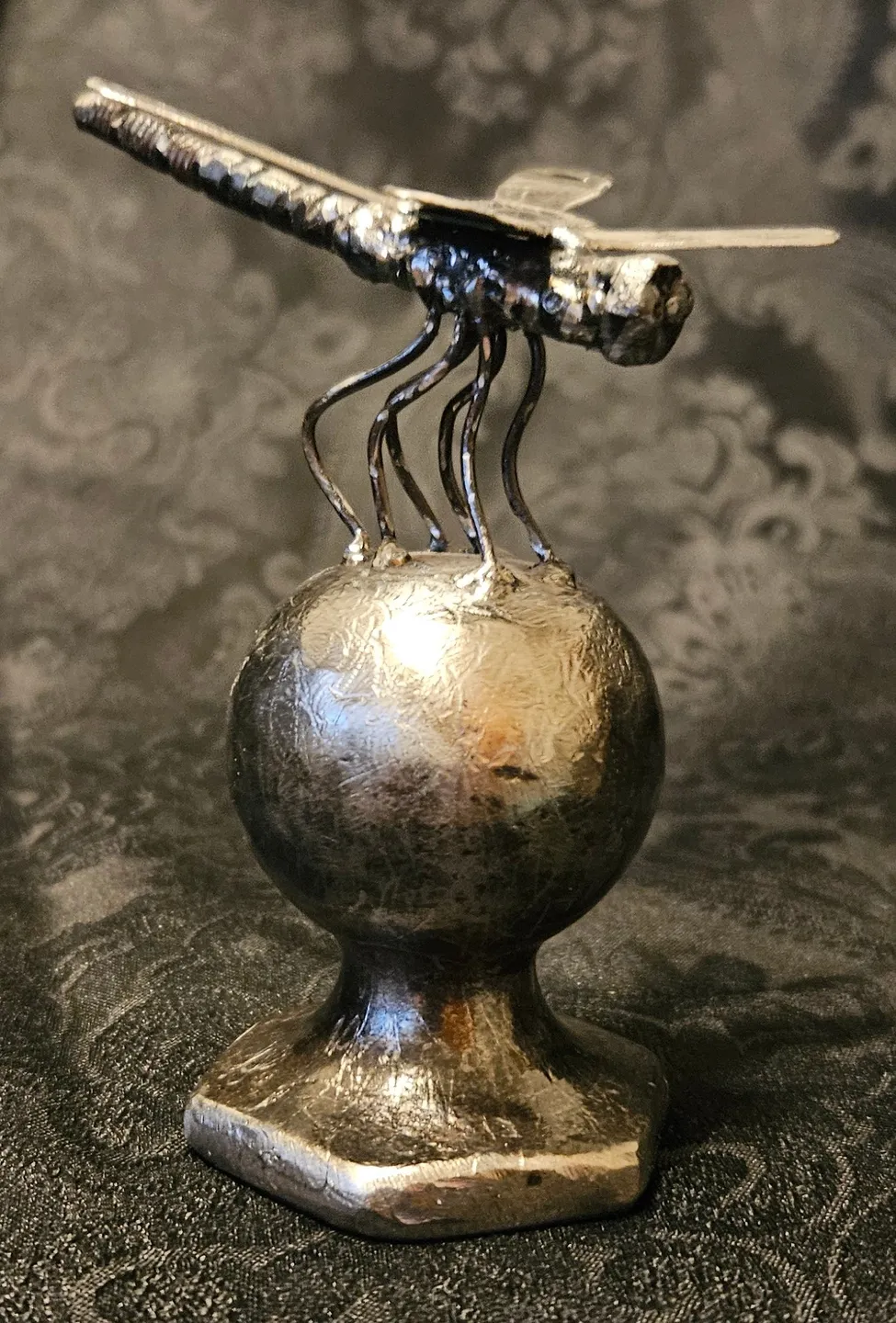 A metal sculpture of an ant on top of a ball.