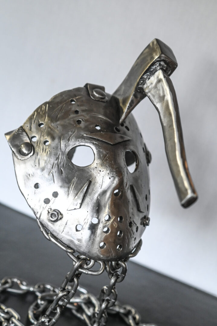 A silver mask with a metal handle hanging from the side of it.