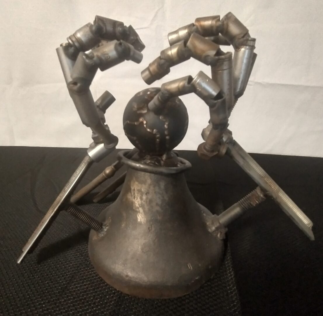 A metal sculpture of hands holding onto a teapot.